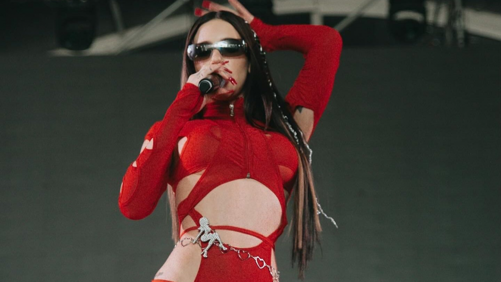 Artista femenina se presenta en vivo durante un festival, vistiendo un outfit rojo sobre el escenario.