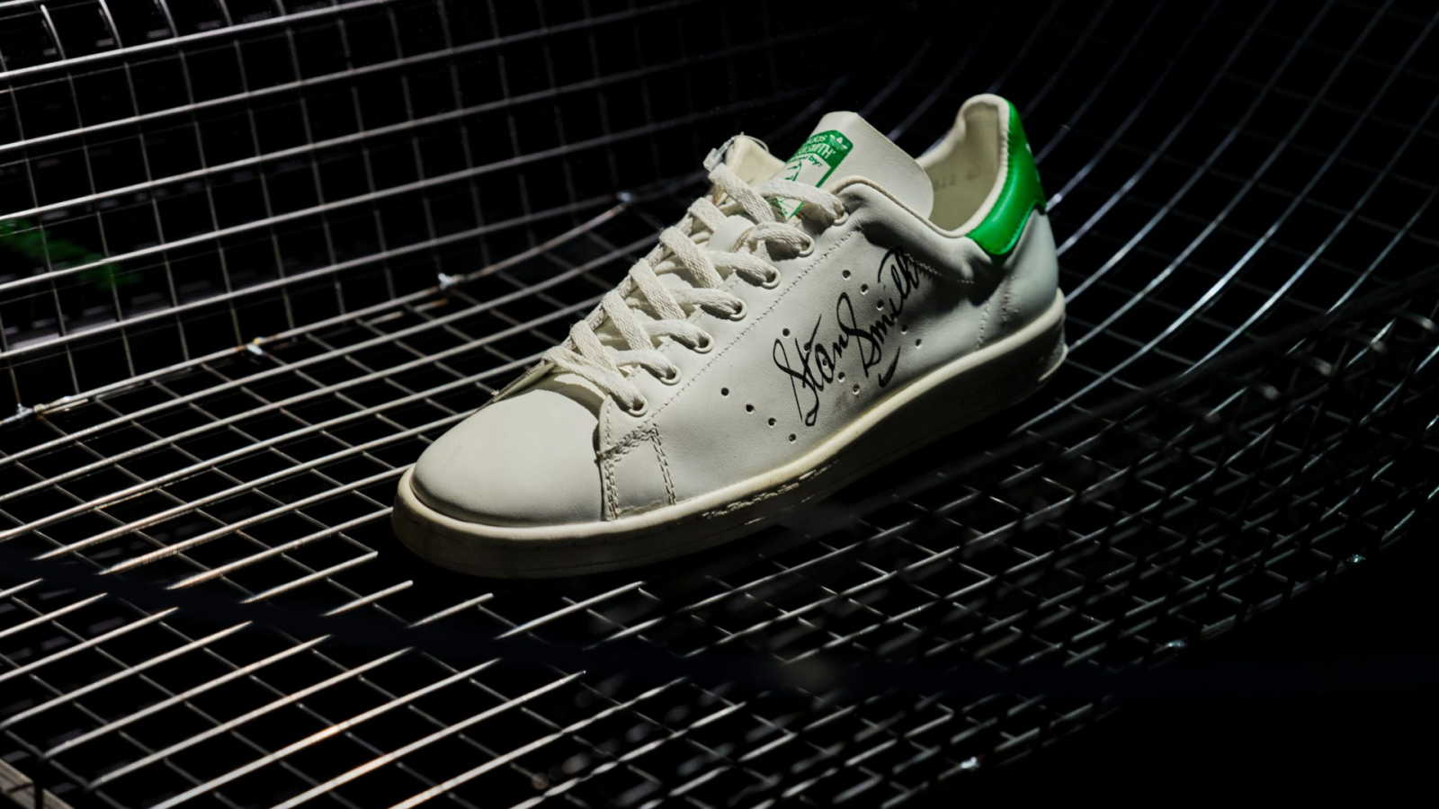 Sneaker blanco con detalles verdes fotografiado sobre estructura metálica negra en iluminación oscura