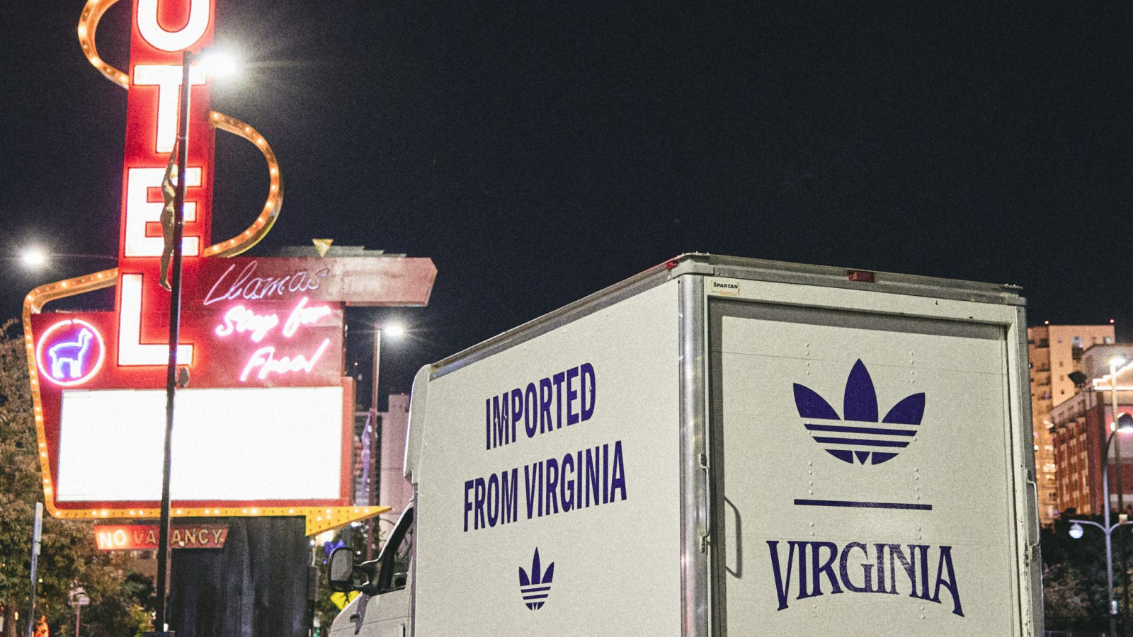 Camión con branding VIRGINIA de Pharrell Williams y adidas Originals estacionado frente a un motel con letrero neón, promocionando las Adistar Jellyfish.