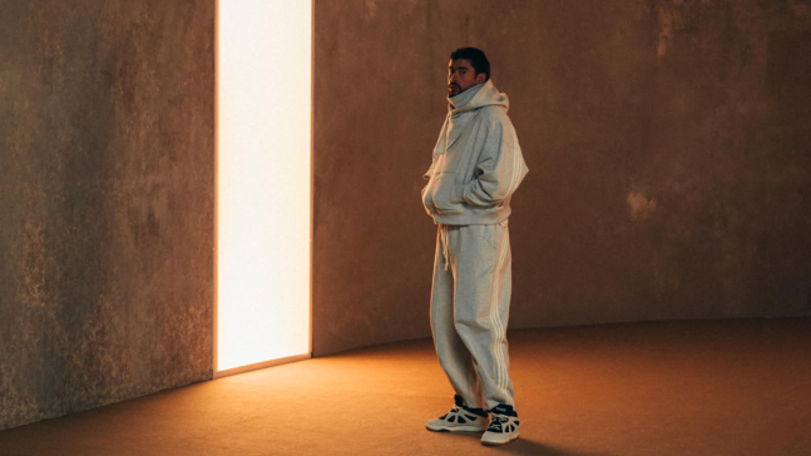 Bad Bunny con conjunto deportivo de adidas Originals y sneakers BadBo 1.0 en un espacio minimalista con iluminación vertical