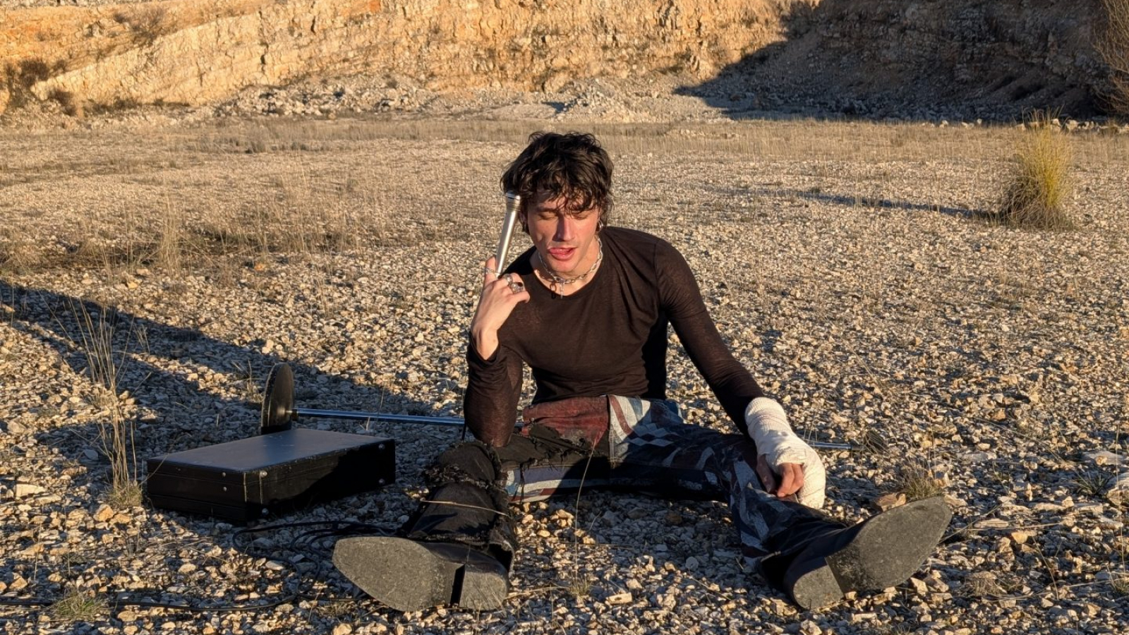 Pol Granch sentado en un paisaje árido y rocoso durante una sesión fotográfica del lanzamiento de “pecos”.