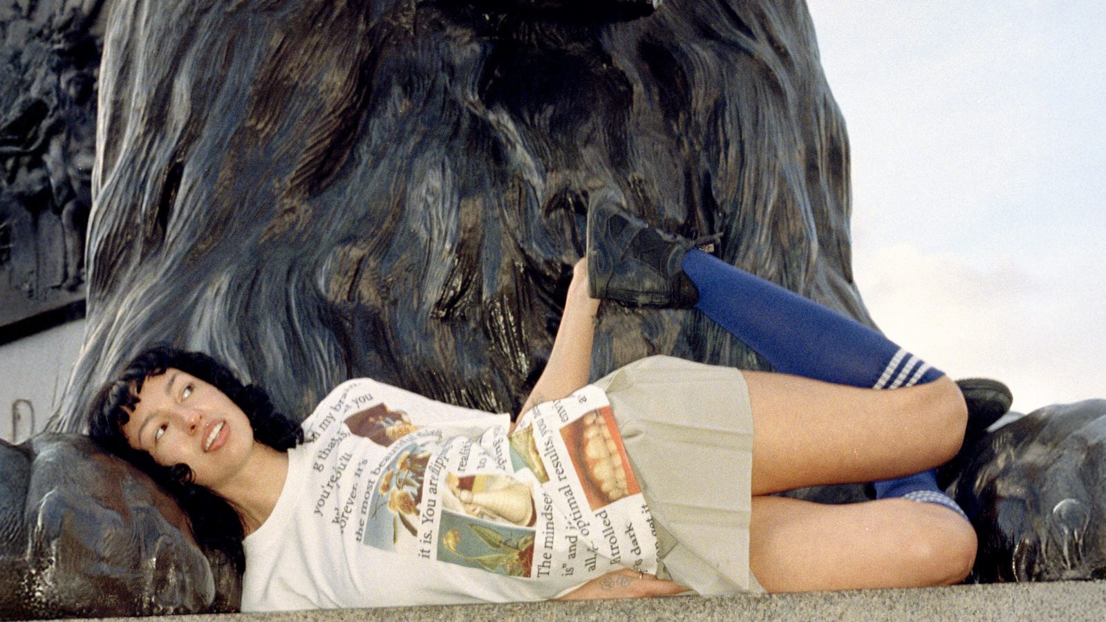Modelo recostada frente a escultura de león en Londres vistiendo look de la colección PLEASURES Spring 2026
