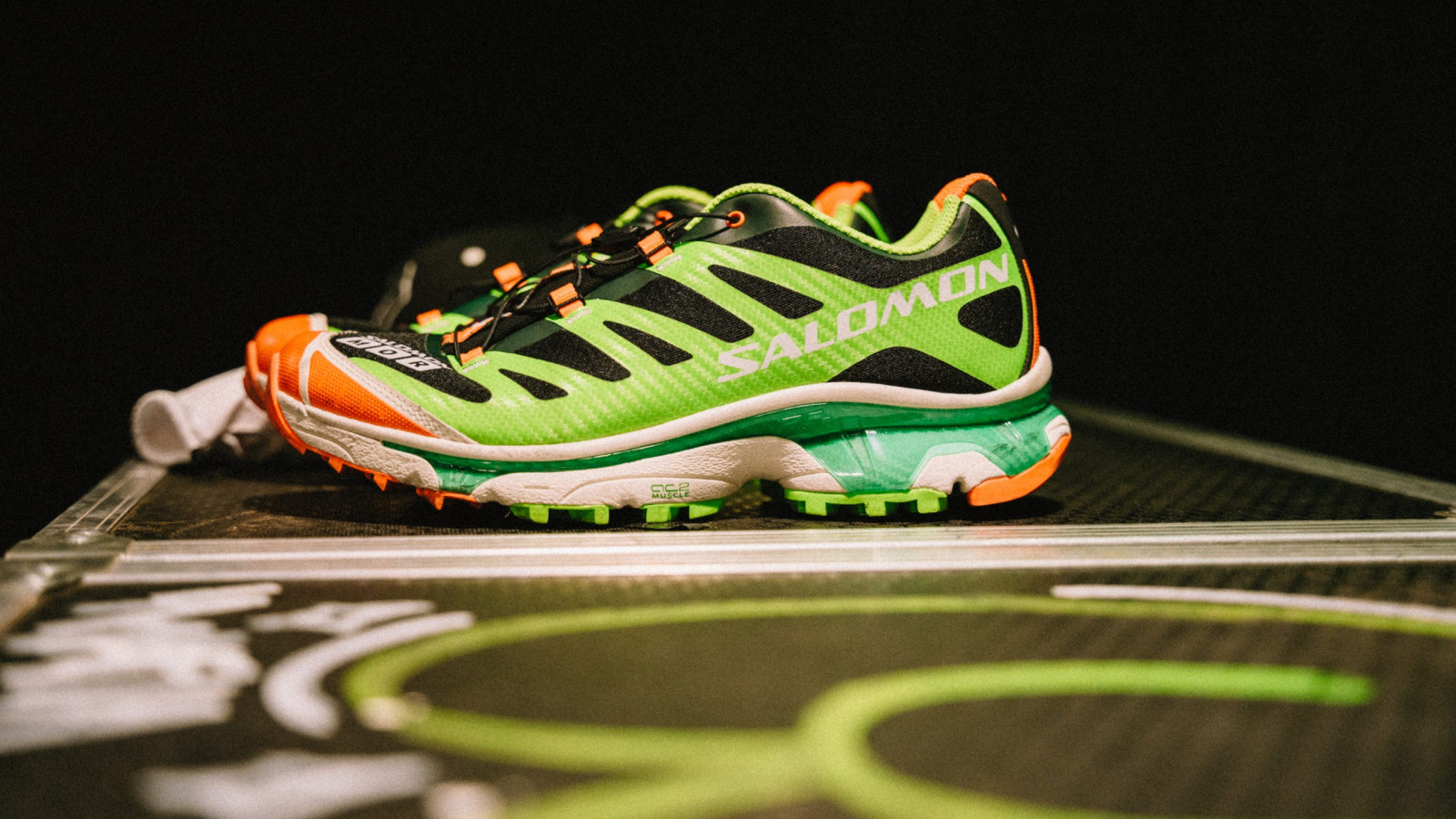 Sneaker Salomon XT-4 OG “Ferxxocalipsis” en tonos verde neón, negro y naranja, inspirado en el universo visual de Feid y exhibido sobre una plataforma.