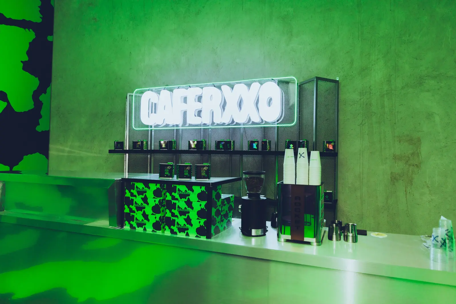 Barra de CAFERXXO con letrero luminoso y acentos verdes dentro del pop-up de Salomon y Feid.