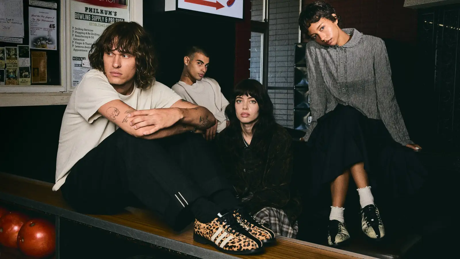 Cuatro personas en la zona de asientos de un boliche lucen los zapatos adidas x Brain Dead Bowling con estampados de leopardo y serpiente.