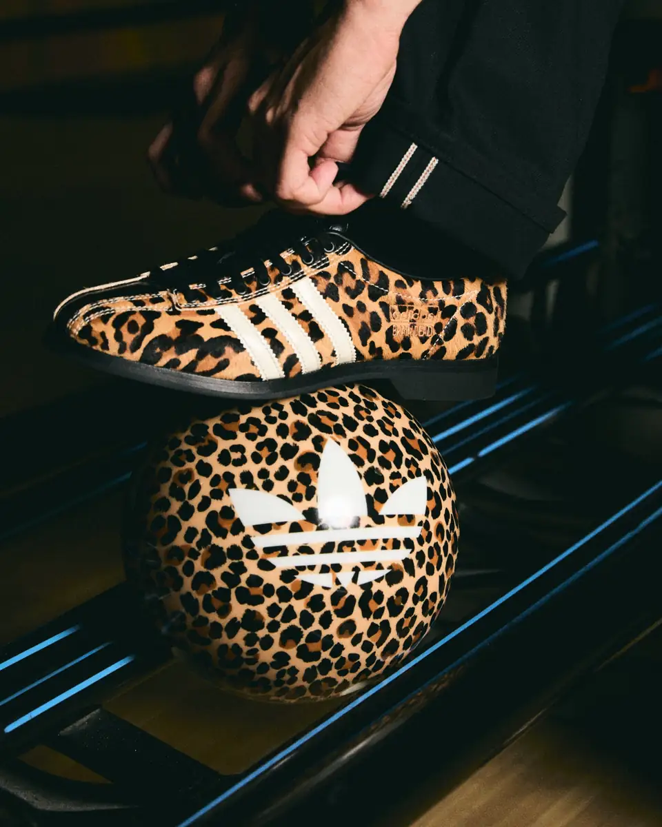 Detalle del zapato adidas x Brain Dead Bowling con estampado de leopardo y tres franjas blancas, sobre una bola de bolos con estampado de leopardo.