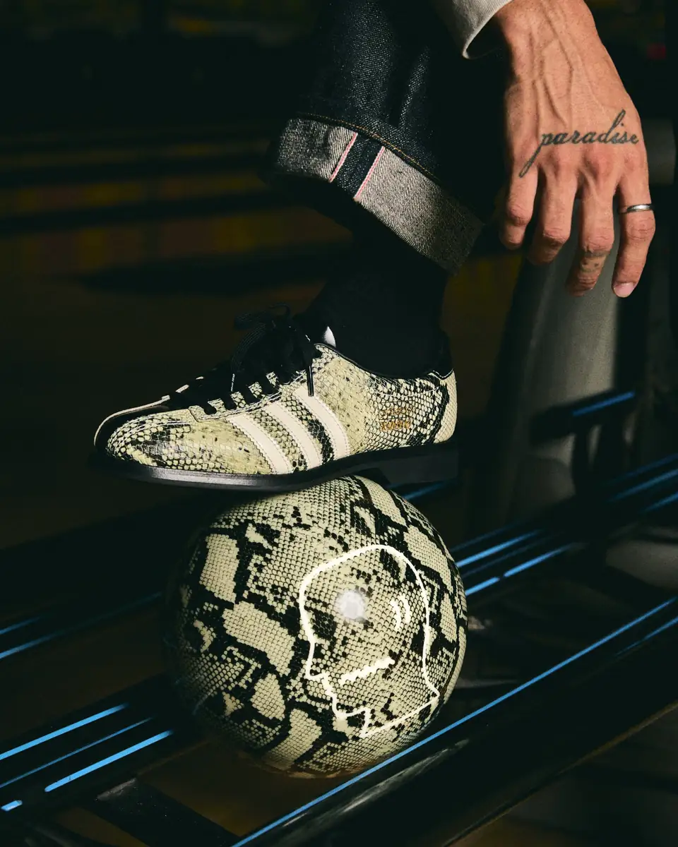 Detalle del zapato adidas x Brain Dead Bowling con acabado de serpiente y tres franjas blancas, apoyado sobre una bola de bolos con el mismo patrón.