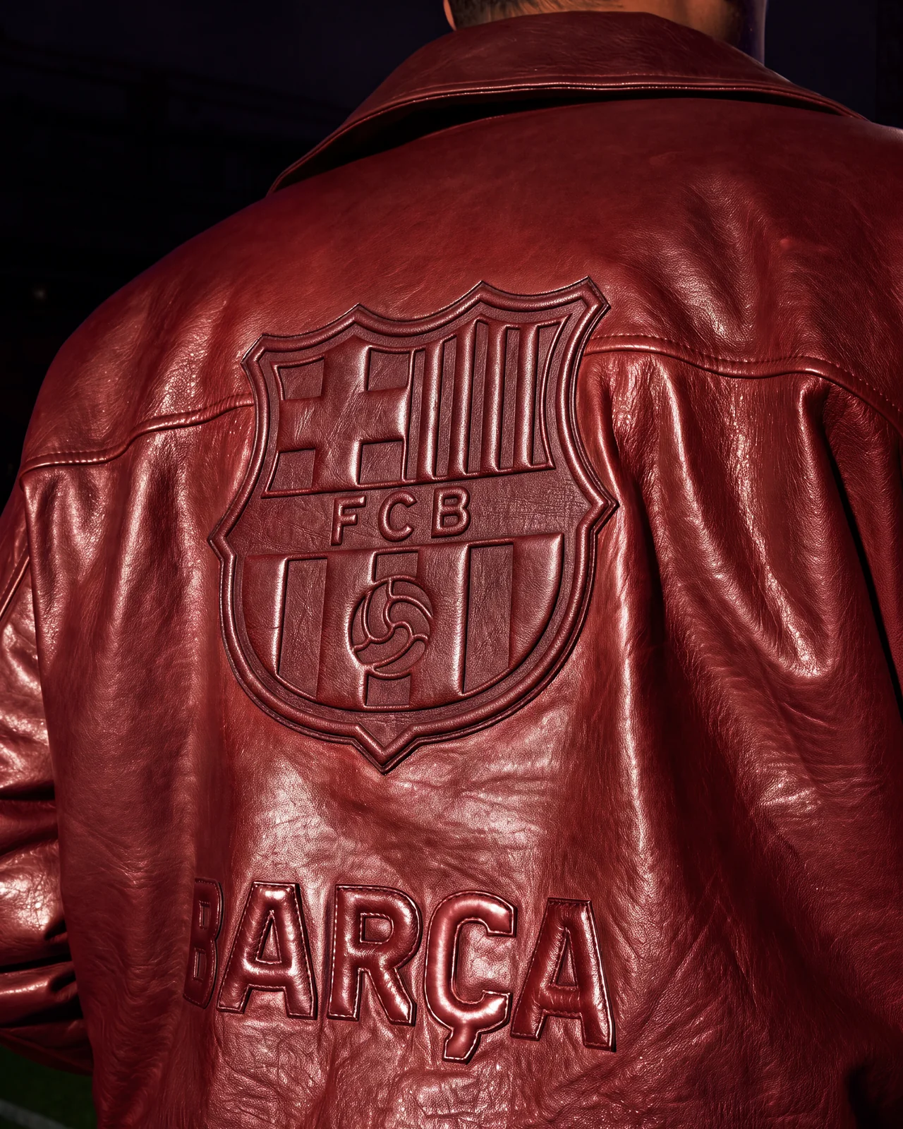 Relief-embossed FC Barcelona crest and Barça lettering on the back of a garnet leather AMIRI jacket.