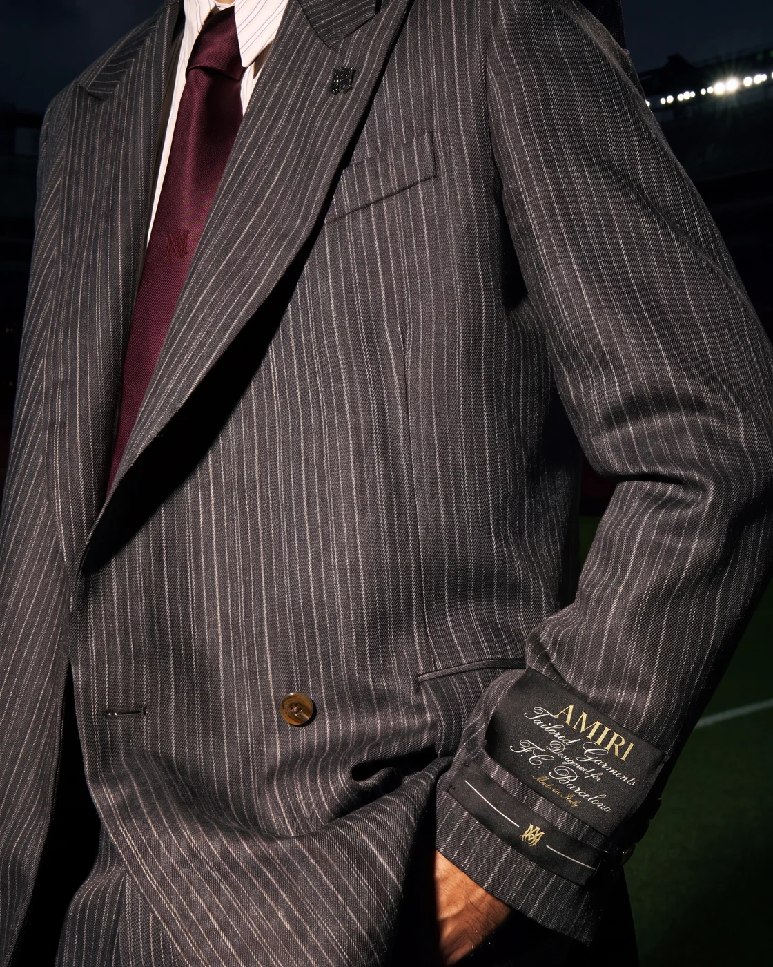 Close-up of an AMIRI grey multi-striped double-breasted jacket worn with a striped shirt and garnet tie.