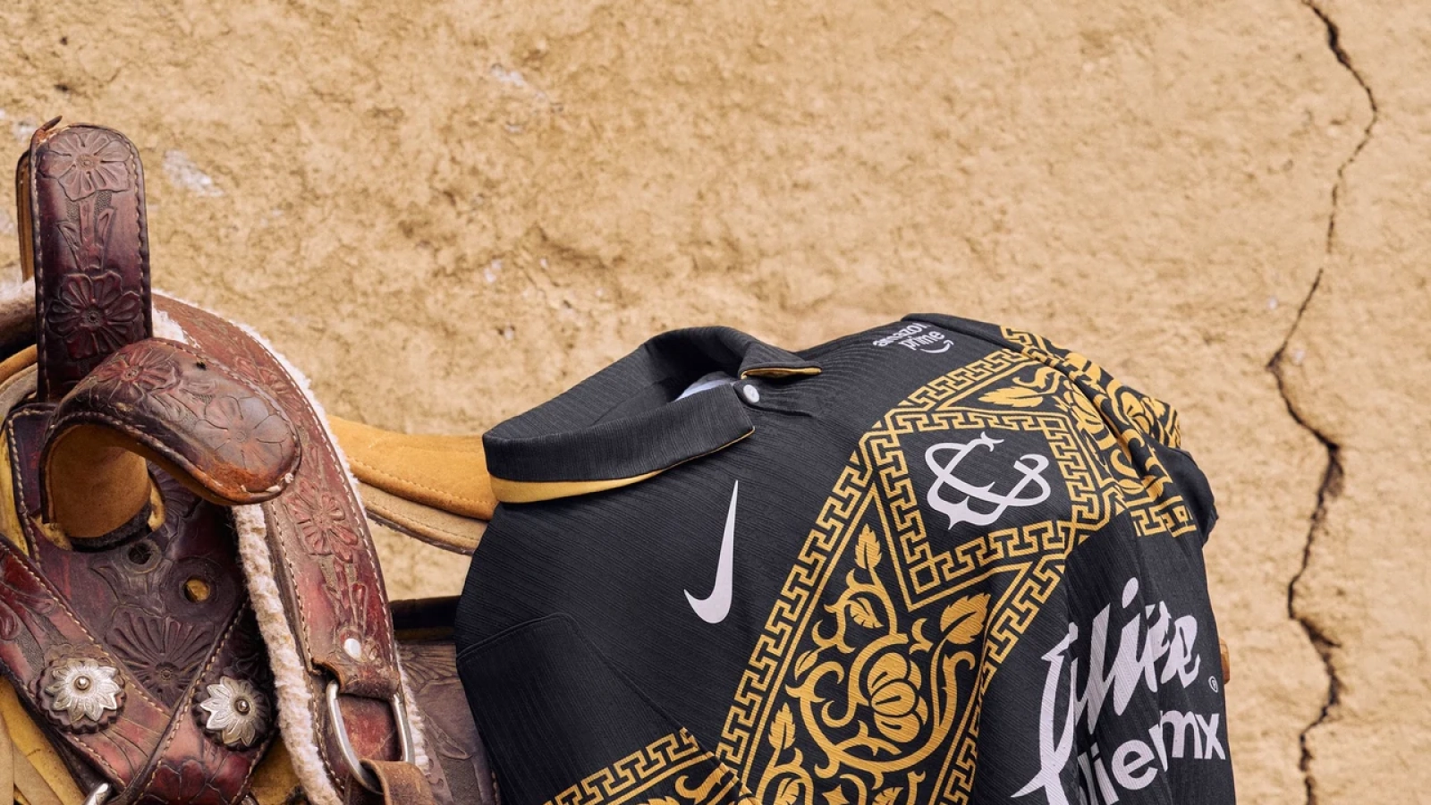 Jersey negro de Chivas con patrón dorado junto a una silla de montar y un monograma en la pared.
