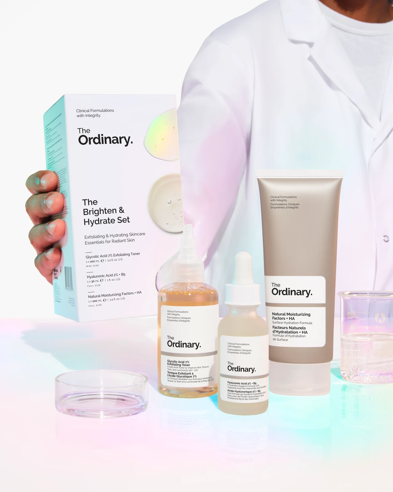 Caja y tres productos de The Brighten & Hydrate Set de The Ordinary junto a material de laboratorio.