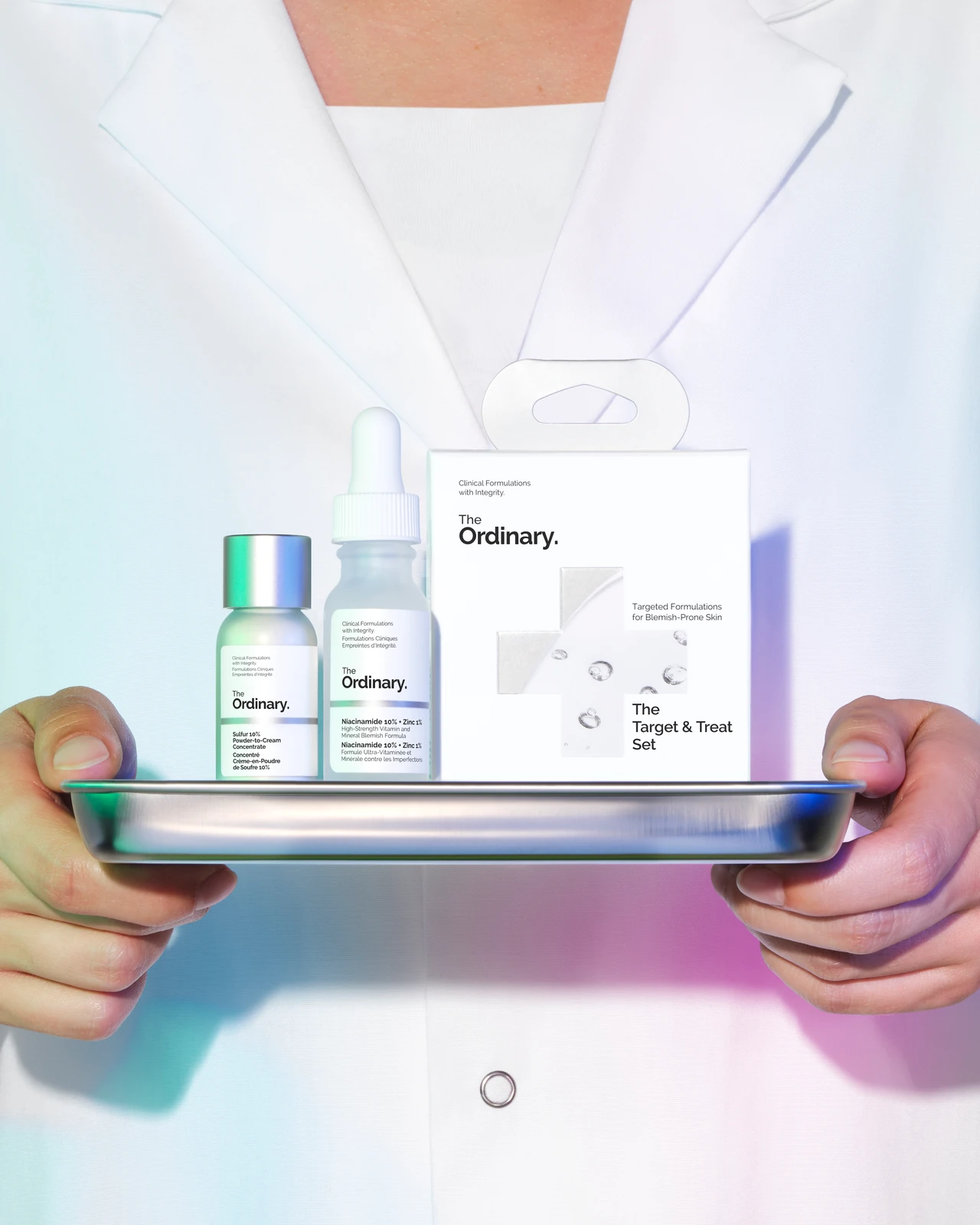 Una persona con bata blanca sostiene una bandeja con The Target & Treat Set de The Ordinary.