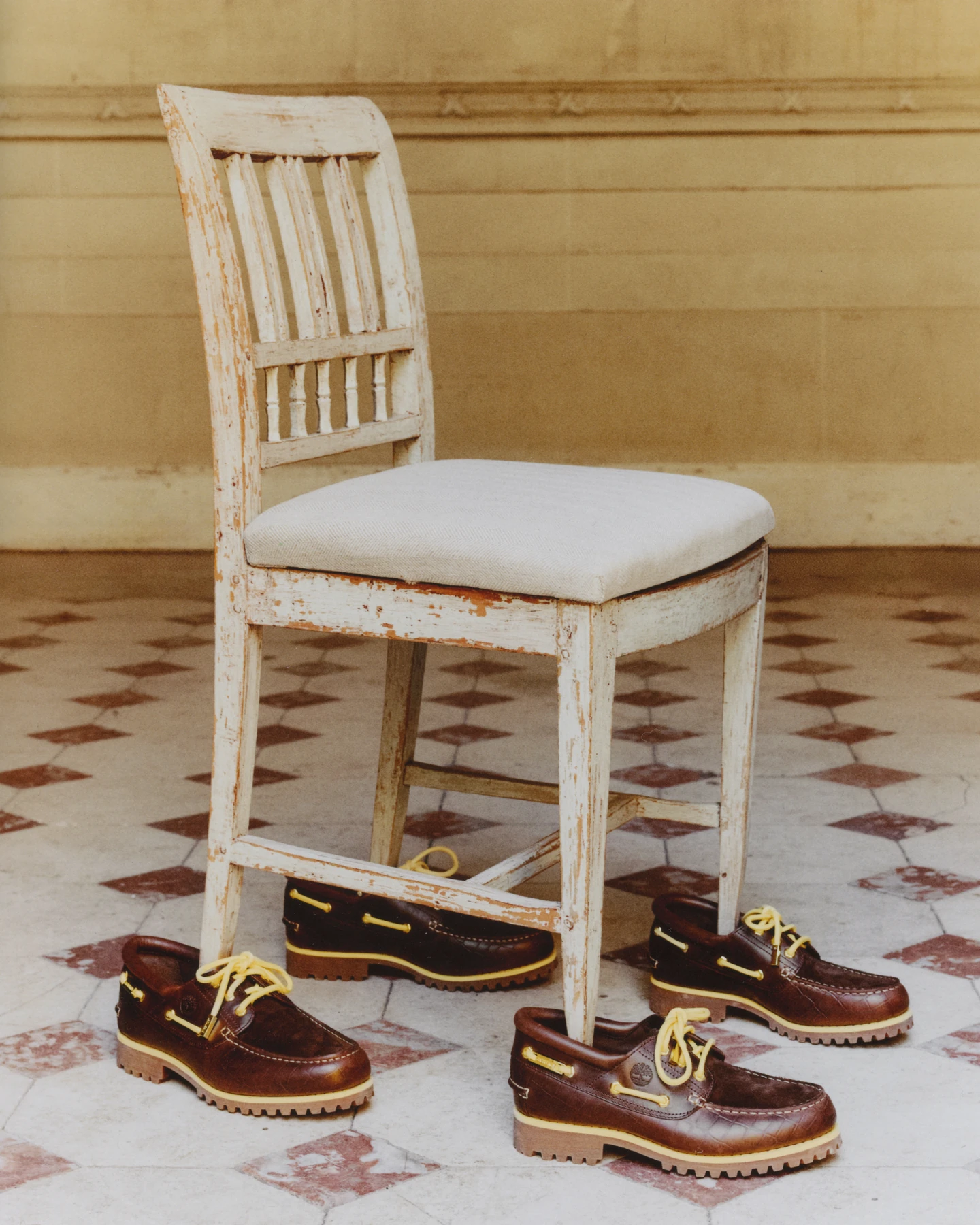 Una silla de madera clara y varios náuticos Timberland x Jacquemus en café sobre un piso de baldosas.